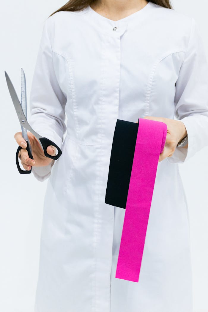 A healthcare professional in a white coat holding kinesiology tape and scissors on a white background.